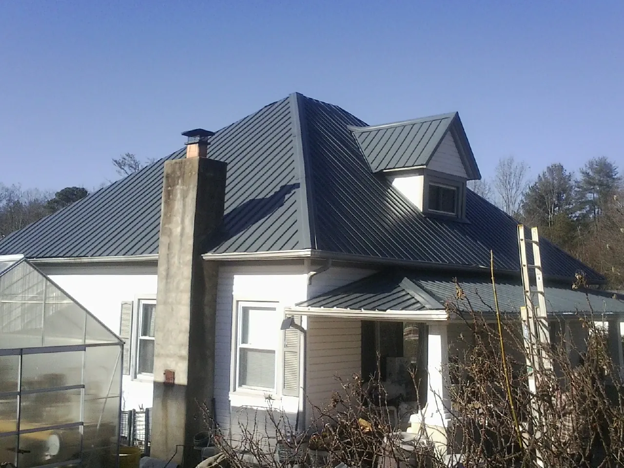 Dark blue standing seam metal roof on a white farmhouse with dormer — Slate & Tile Roof Repair by Roofing Brothers in Noonan