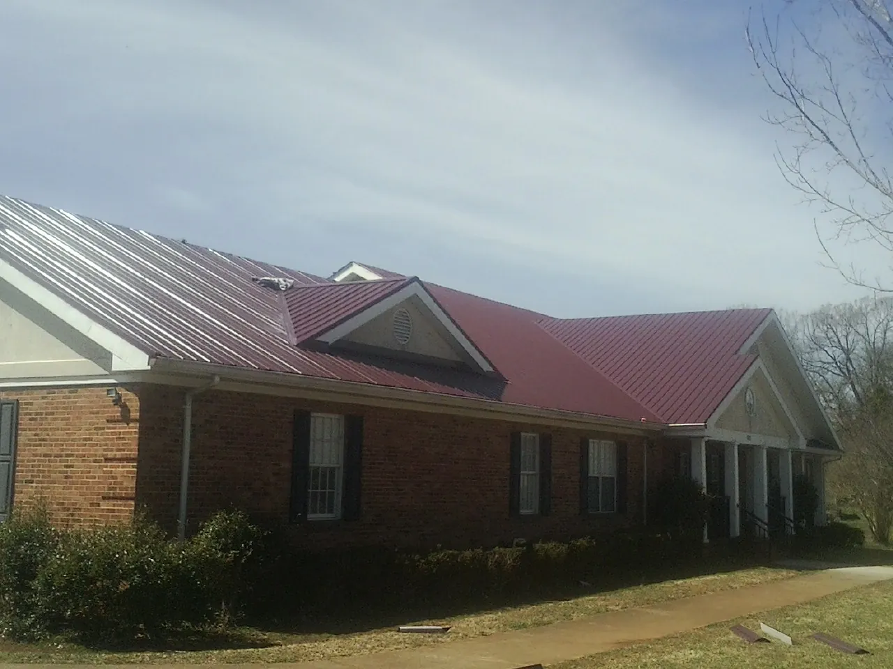 Red metal roof with gabled entries on a long brick building, from a Hail Damage Roof Repair job in Noonan