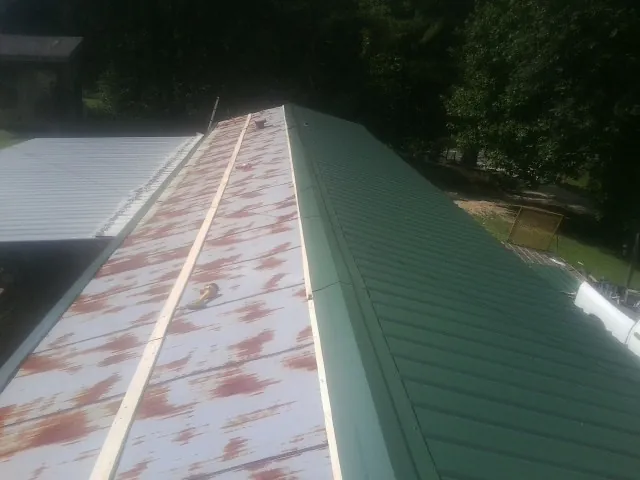 Old rusted panels beside newly installed green metal roofing — Wind Damage Roof Repair by Roofing Brothers in Noonan