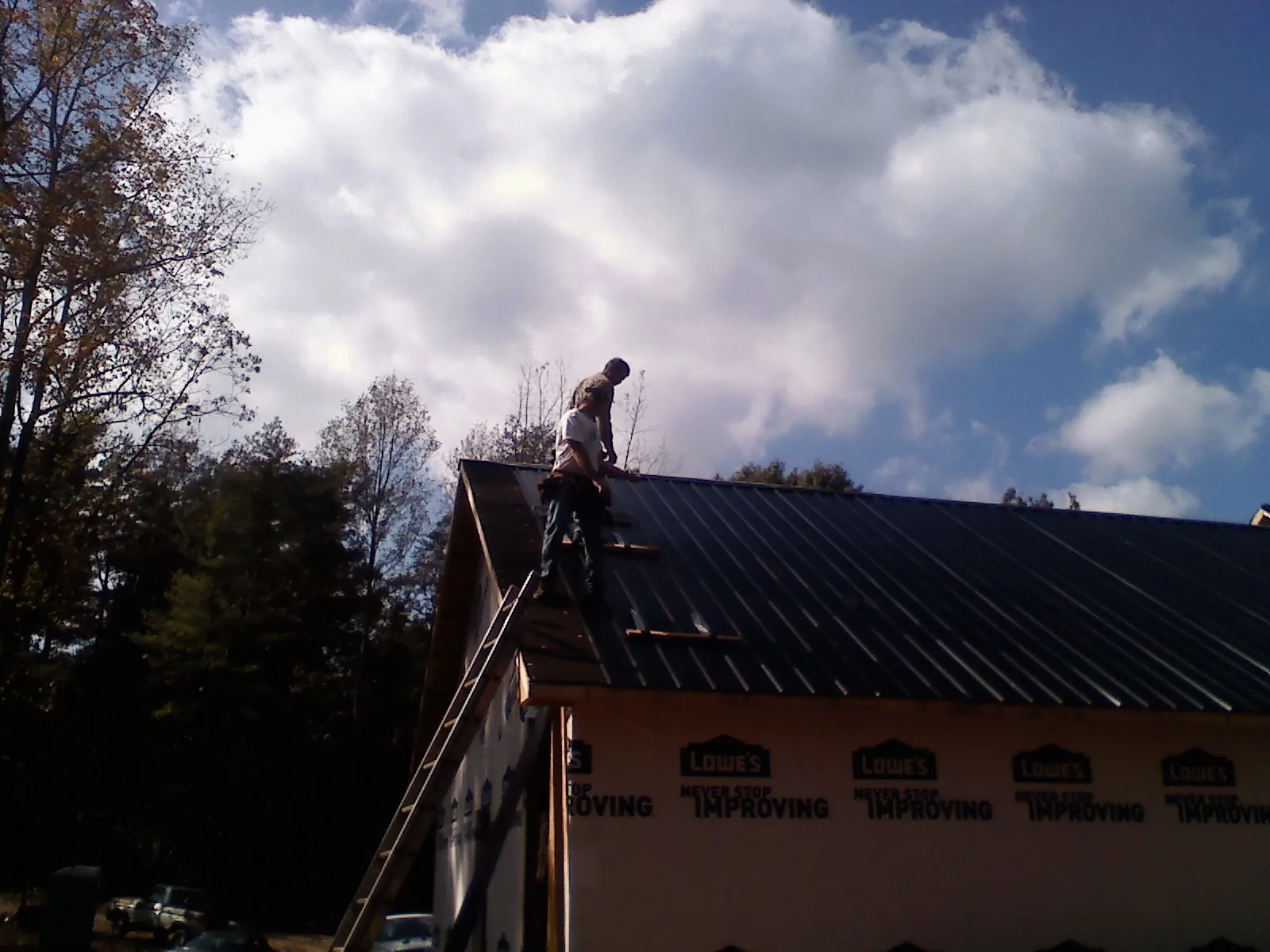 Roofer fastening dark metal panels high against a cloudy sky, from a Roof Inspection job in Noonan