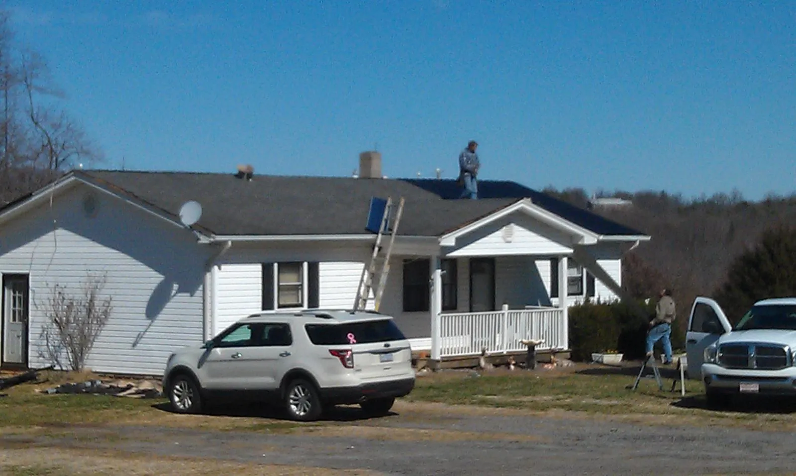 Roofers stripping shingles from a white ranch house roof in Noonan
