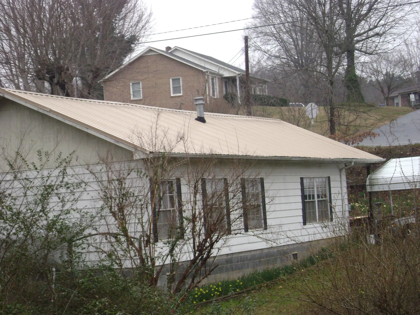 Tan metal roof on a white sided house set into a hillside — Commercial Roofing by Roofing Brothers in Noonan