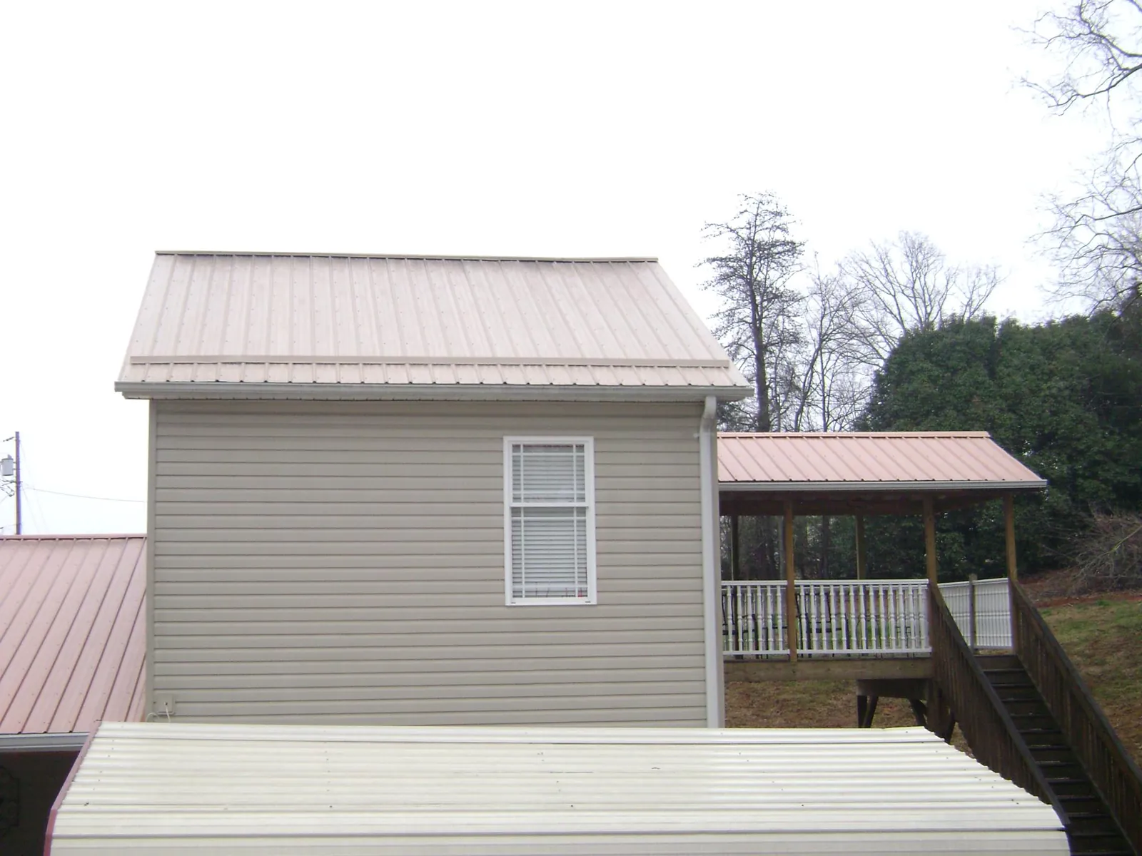 Tan metal roofs on a two story addition and attached porch, from a Roof Replacement job in Noonan
